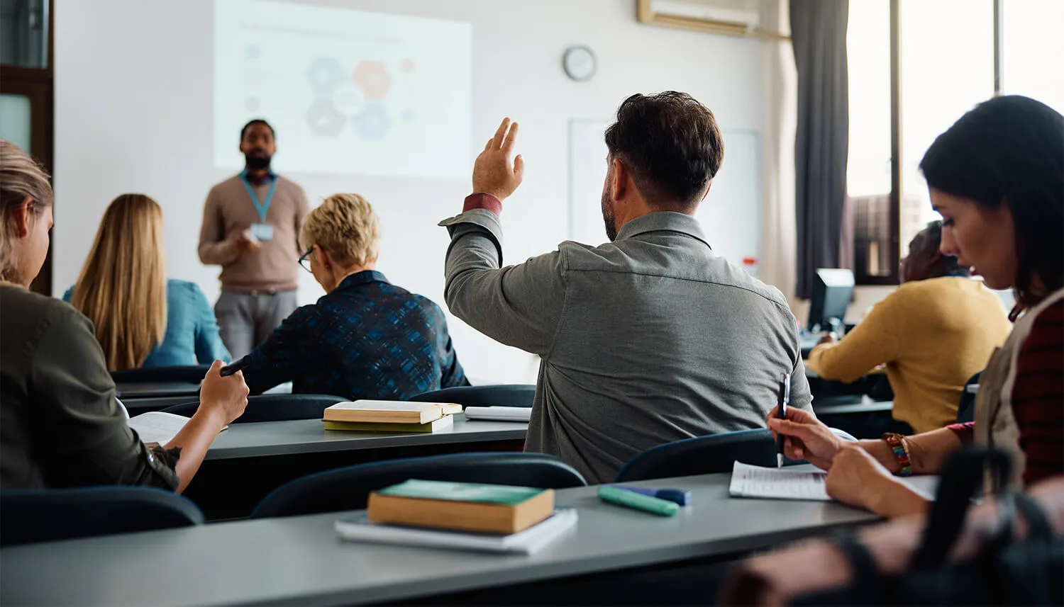 college students in a classroom student raises hand in question in a classroom